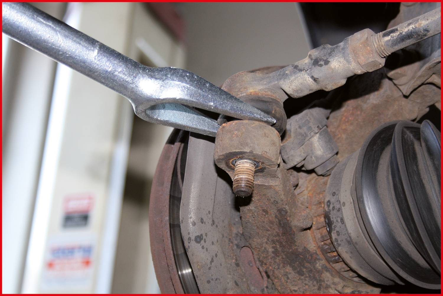 Nahaufnahme eines rostigen Autoteils, wobei ein Werkzeug benutzt wird, um eine Schraube zu lösen. Das Werkzeug greift an einer Mutter an.