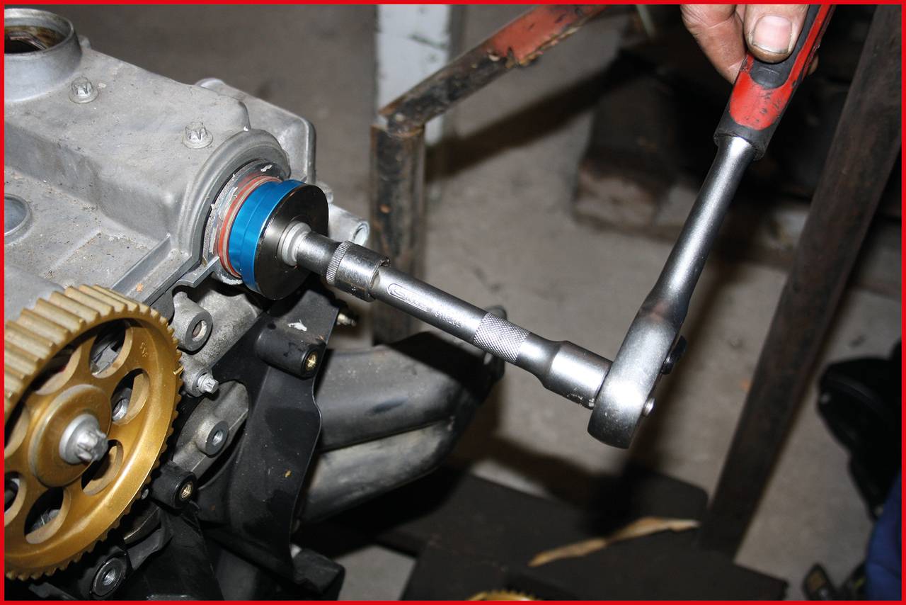 'Person zieht eine Schraube mit einer Ratsche an einem Motorteil fest.'