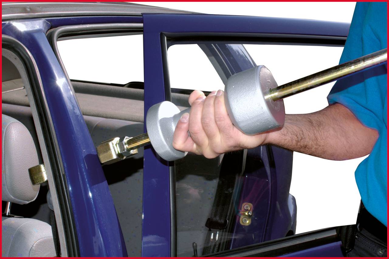 Eine Person bricht mit einem Werkzug in ein Auto ein, indem sie das Schloss der Vordertür aufbricht.