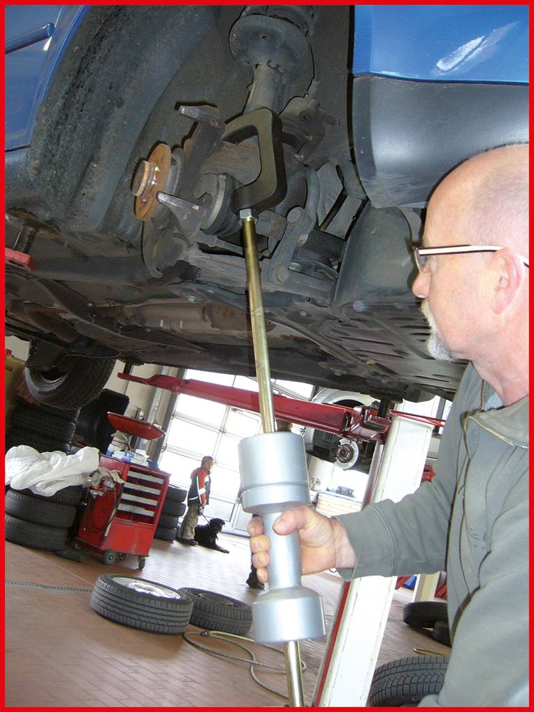 Ein Mechaniker arbeitet an der Aufhängung eines Autos in einer Werkstatt. Das Auto ist auf einer Hebebühne angehoben, und Werkzeuge liegen bereit.