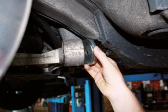 Eine Hand führt eine mechanische Untersuchung an einem Autoteil unter einem Fahrzeug durch, das auf einer Hebebühne angehoben ist.