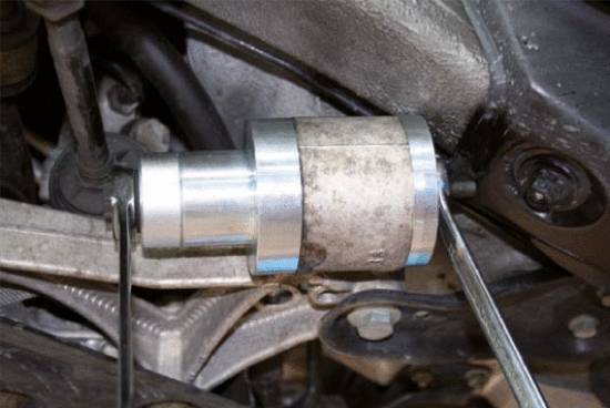 Ein montiertes Autoteil unter einem Fahrzeug. Eine Metallbuchse oder Befestigung mit Schrauben zeigt mechanische Details der Radaufhängung.
