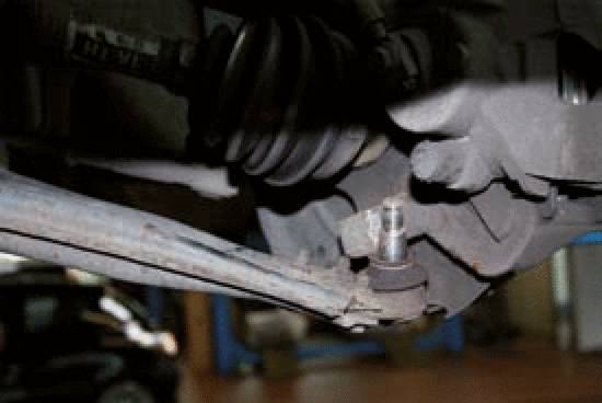 Detailaufnahme eines Autoteils in einer Werkstatt, zeigt eine Federung oder Aufhängungskomponente mit umgebenden mechanischen Teilen.
