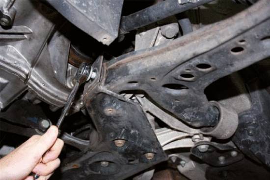 Eine Person zieht eine Mutter mit einem Schraubenschlüssel an der Fahrzeugunterseite fest, wodurch eine Reparatur oder Wartung angedeutet wird.