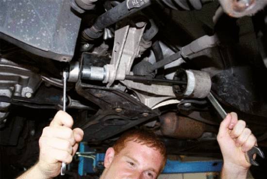 Ein Mechaniker repariert die Aufhängung eines Autos von unten. Er verwendet zwei Schraubenschlüssel, während er unter dem Fahrzeug arbeitet.