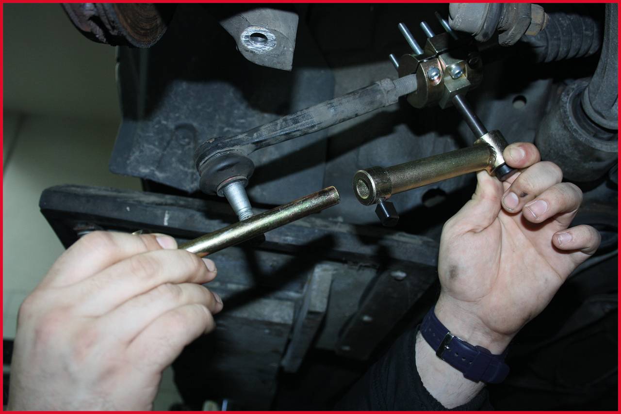 Zwei Hände arbeiten an der Befestigung einer Metallstange unter einem Fahrzeug. Werkzeug wird benutzt. Reparatur oder Wartungsszene.