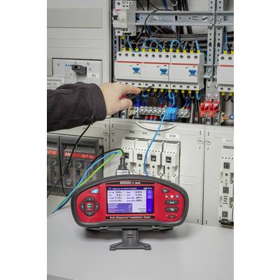 Ein Elektriker benutzt ein elektrisches Prüfgerät vor einem geöffneten Schaltschrank, um die Verkabelung zu überprüfen.