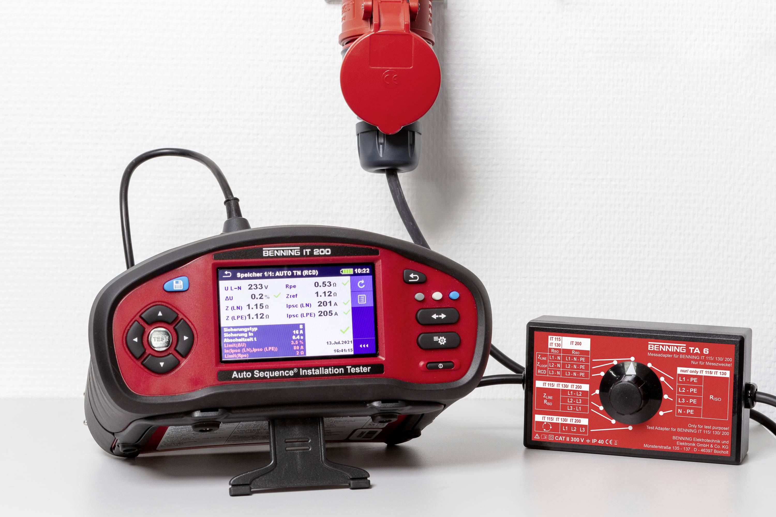 Gerät zur Überprüfung von elektrischen Schaltungen mit digitalem Display, zeigt Messergebnisse an. Anschluss an rote Steckdose im Hintergrund.