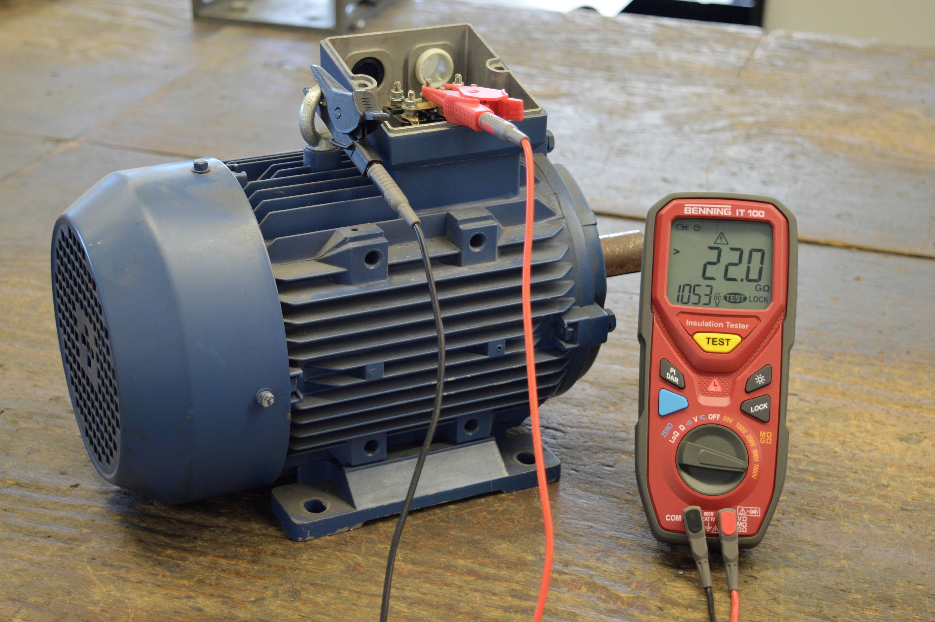 Ein Elektromotor mit einem Multimeter misst eine Spannung von 22,0 V. Das Multimeter ist neben dem Motor auf einem Tisch platziert.