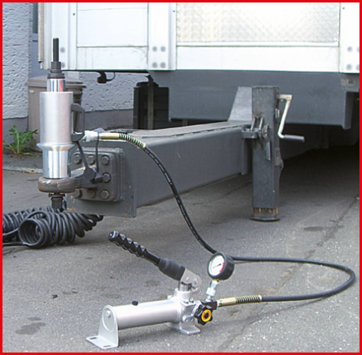 Ein hydraulischer Wagenheber hebt den Anhänger eines Lastwagens an. Ein Messgerät zeigt den Druck an.