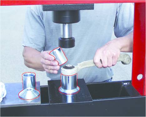 Eine Person bedient eine Metallpresse, um einen zylindrischen Metallgegenstand zu formen. Ein fertiges Teil steht daneben.