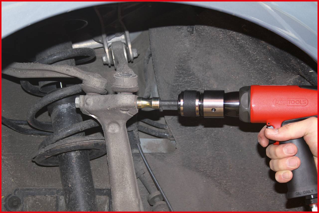 Ein Akkuschrauber wird verwendet, um eine Schraube an einem Fahrzeugfahrwerk zu befestigen. Die Hand einer Person hält das Werkzeug.