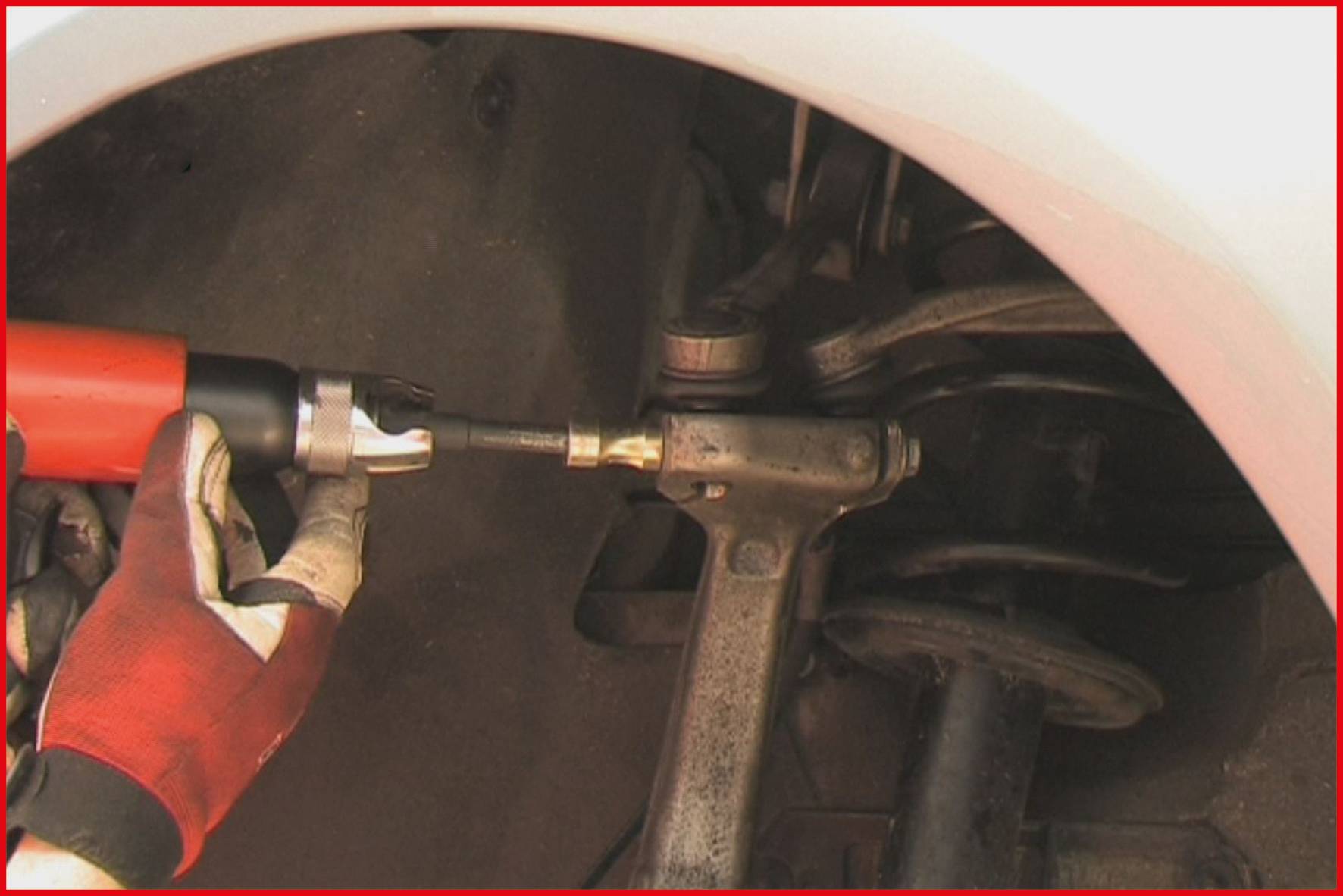 'Eine Person repariert oder wartet ein Autoteil mit einem Werkzeug. Das Bild zeigt einen Nahbereich der Federung eines Fahrzeugs.'