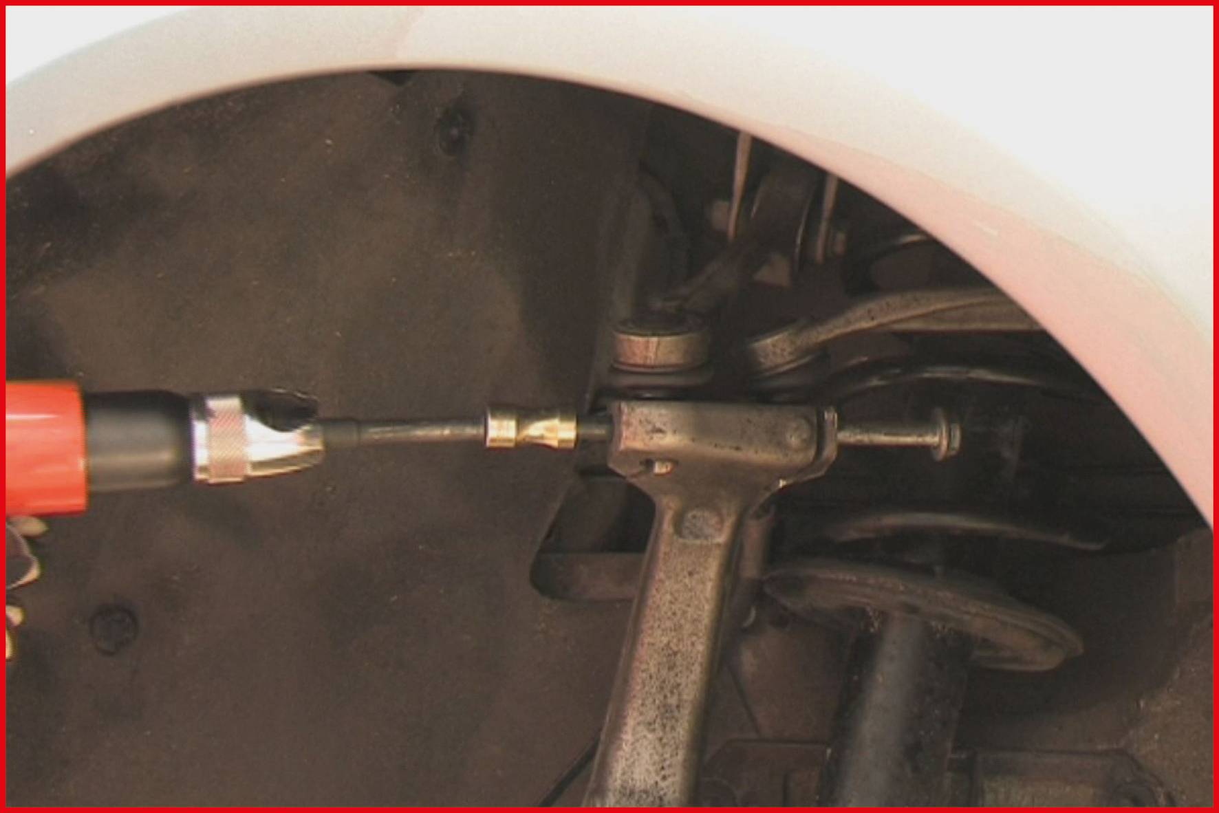 Ein Mechaniker schraubt ein Autoteil im Radkasten an. Ein roter Bohrschrauber wird verwendet, um die Verbindung zu sichern.