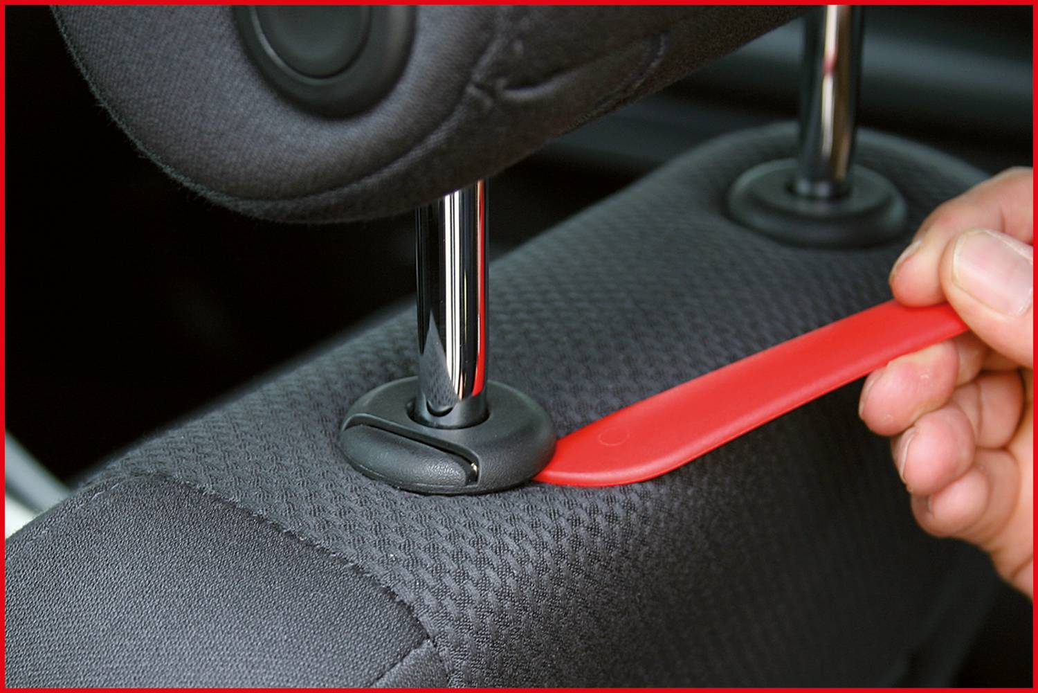 Eine Hand verwendet ein rotes Werkzeug, um die Kopfstütze eines Autositzes zu entfernen.