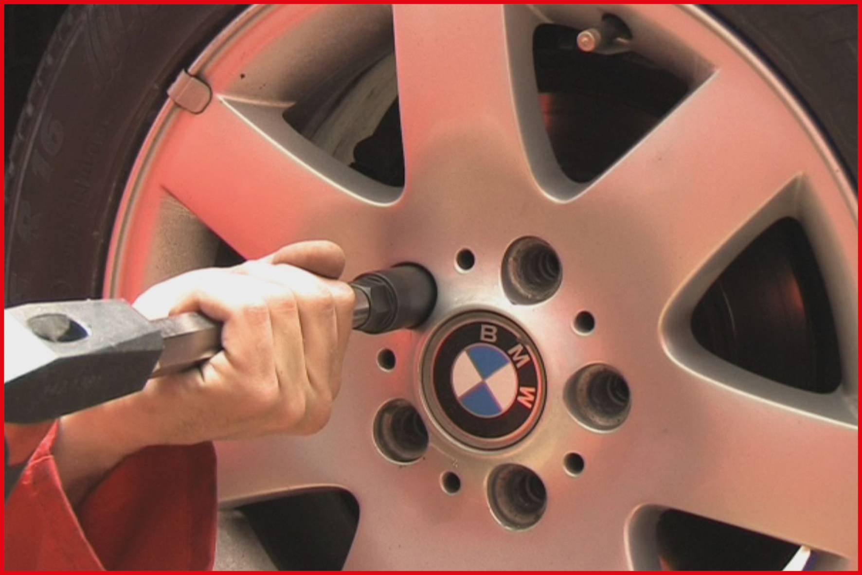 Eine Person zieht Schrauben an einem Autoreifen mit einer Radkappe mit BMW-Logo fest.