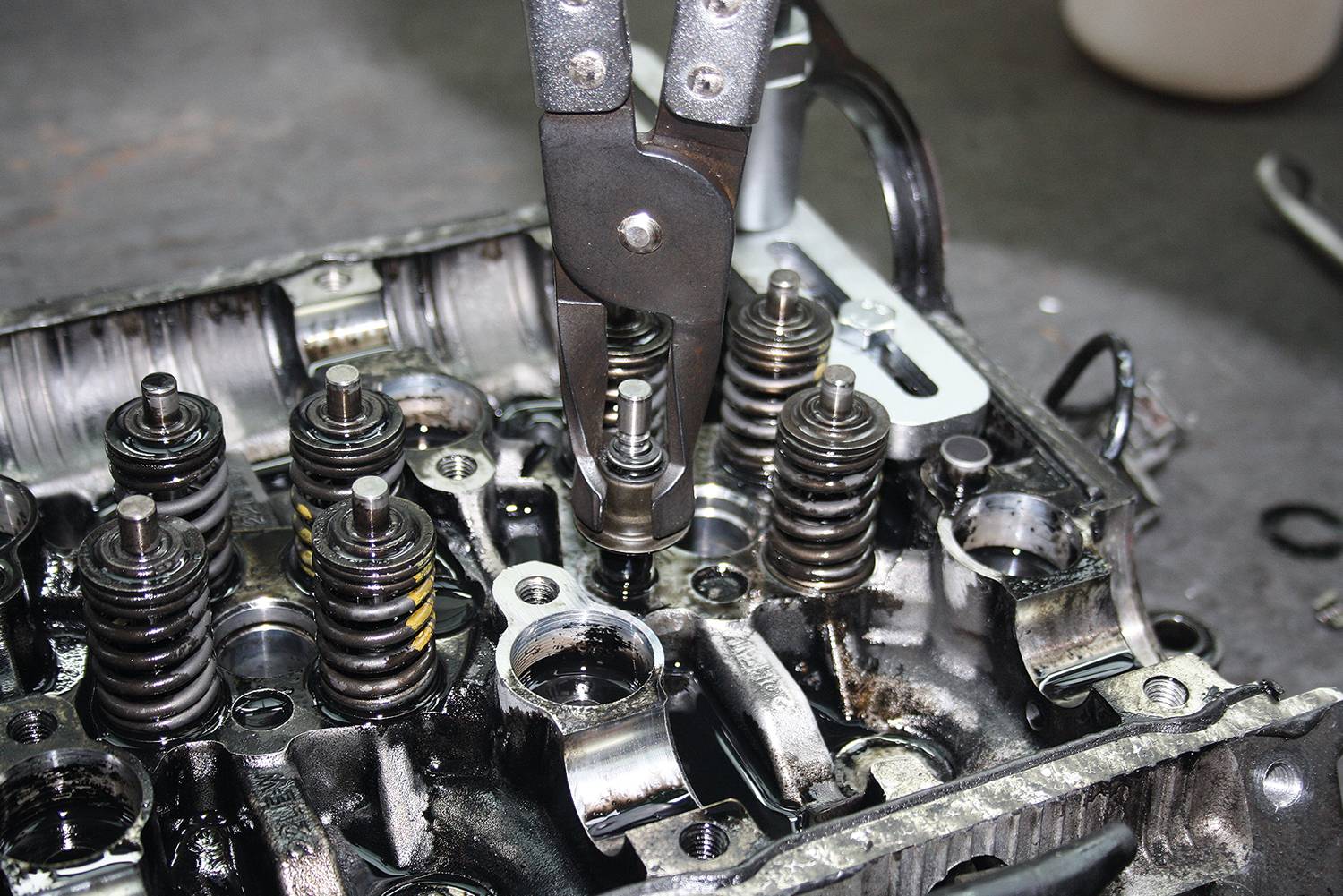 Ein Mechanikerwerkzeug entfernt ein Ventil aus einem Motorblock. Mehrere Federn und Metallkomponenten sind sichtbar.