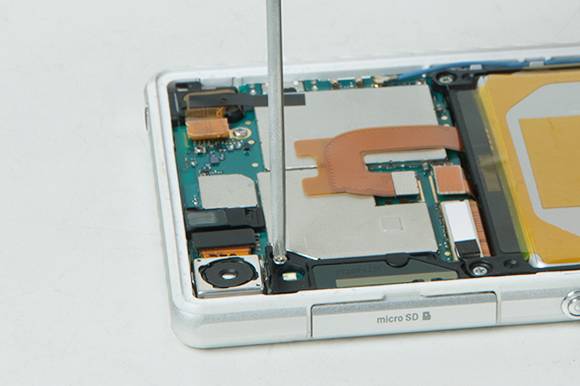 Eine Hand benutzt einen Schraubendreher, um ein Smartphone zu öffnen. Sichtbar sind innenliegende elektronische Komponenten und ein Steckplatz für microSD.
