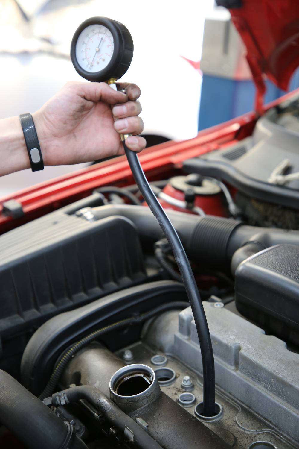 'Eine Hand hält ein Manometer über einem offenen Motor eines Autos, um den Druck zu überprüfen. Die Motorhaube ist geöffnet.'