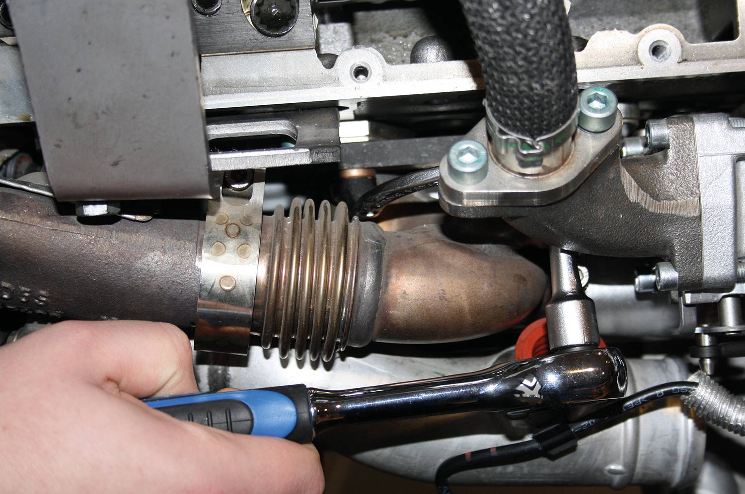 Eine Person zieht eine Schraube an einem Metallrohr eines Motors mit einem Schraubenschlüssel fest.