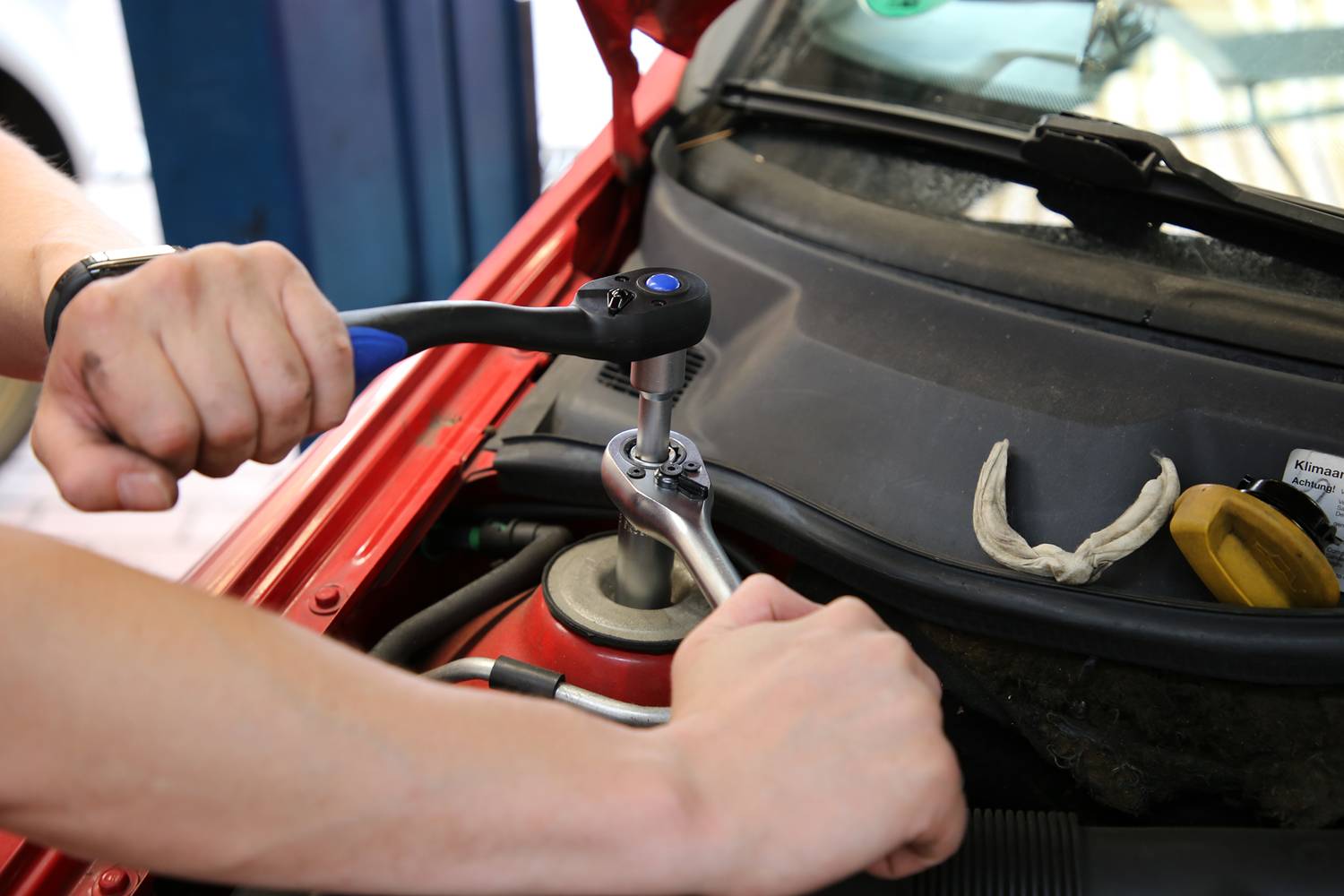 'Person zieht Schraube im Motorraum eines Autos mit einem Schraubenschlüssel an.'