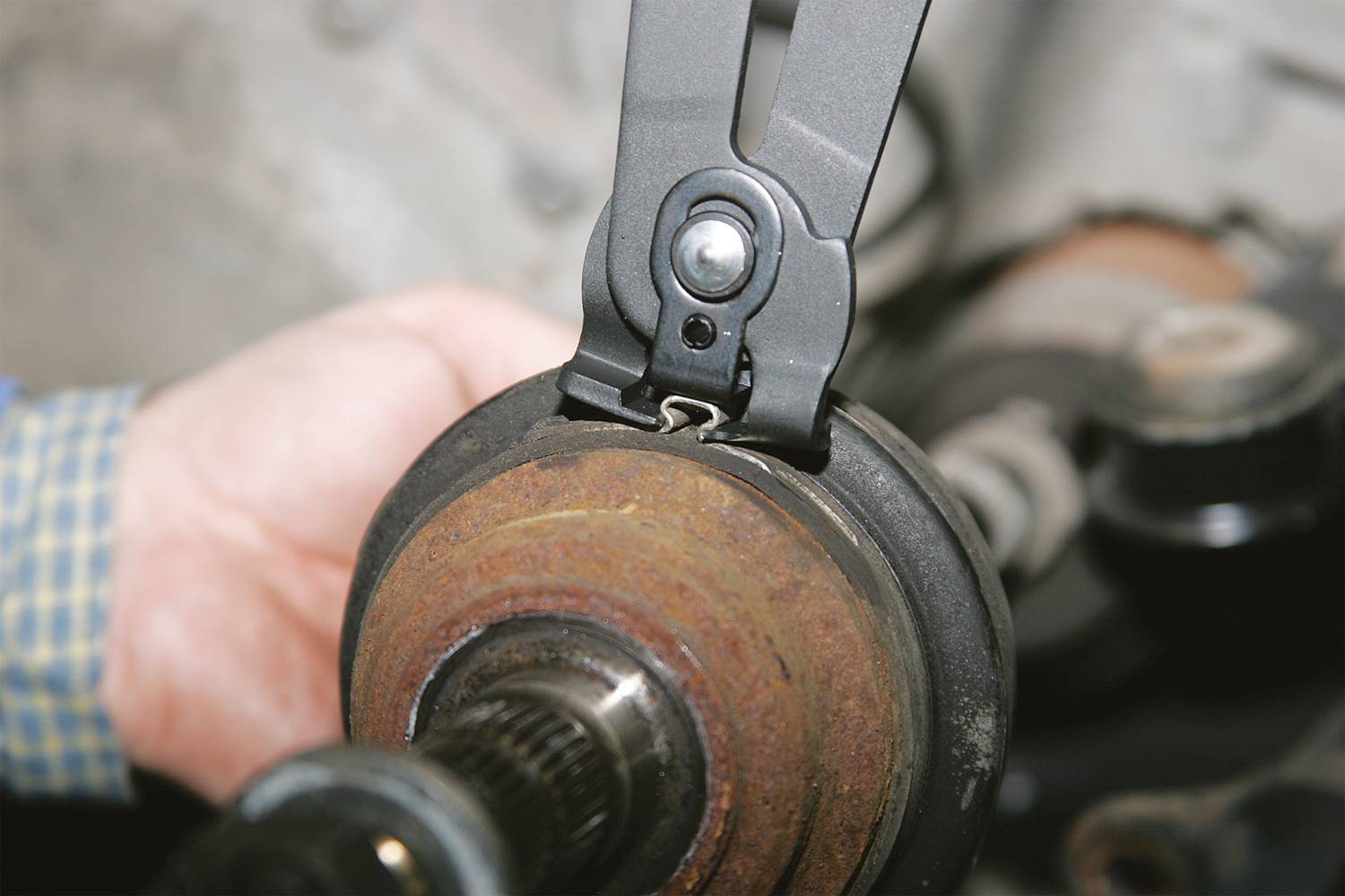 Person hält mit einem Werkzeug eine rostige mechanische Komponente, vermutlich Teil eines Fahrzeugs oder einer Maschine.