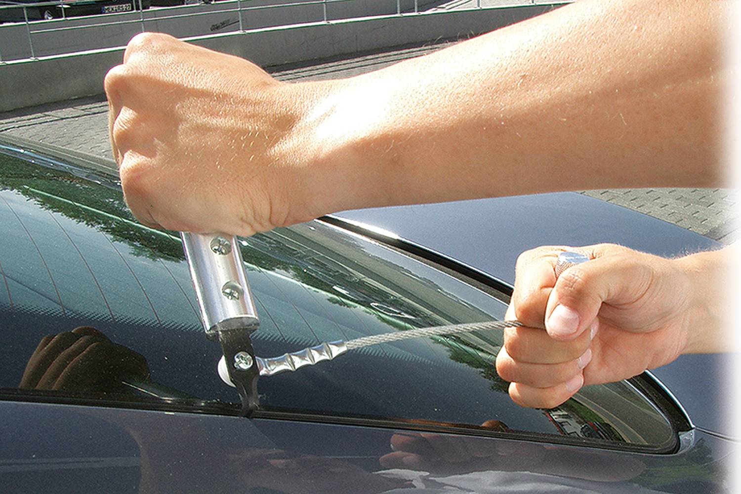 'Zwei Hände zeigen, wie man mit einem speziellen Werkzeug die Gummidichtung eines Autoseitenfensters entfernt. Außenaufnahme.'