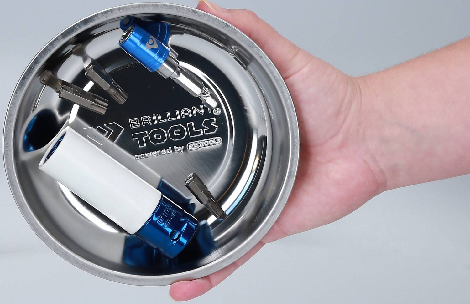 Ein rundes, metallisches Werkzeugtablett wird in einer Hand gehalten. Darin befinden sich Schrauben und blaue Stecknüsse.