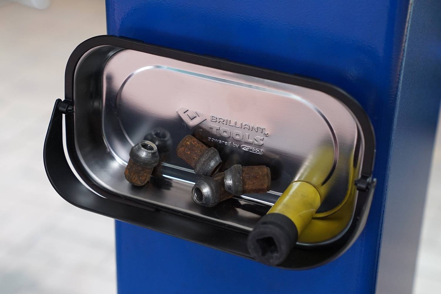 Eine magnetische Schale hält mehrere rostige Schrauben und eine Metallstange. Die Schale ist an einem blauen Metallpfosten befestigt.