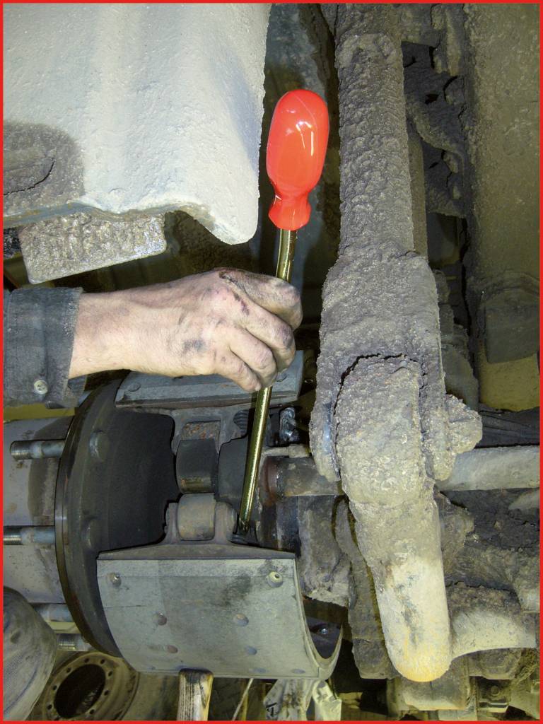 Eine Hand hält einen Schraubendreher, der an einem verschmutzten Maschinenbauteil arbeitet, möglicherweise zur Wartung oder Reparatur.