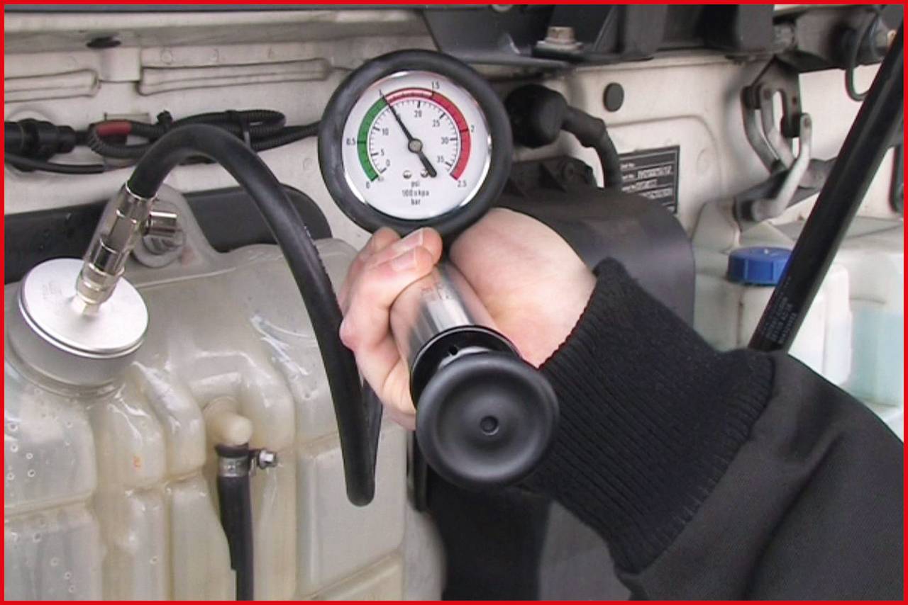Eine Hand hält ein Druckmessgerät, das an einen Motor angeschlossen ist. Das Manometer zeigt Druckwerte im roten, grünen und weißen Bereich.