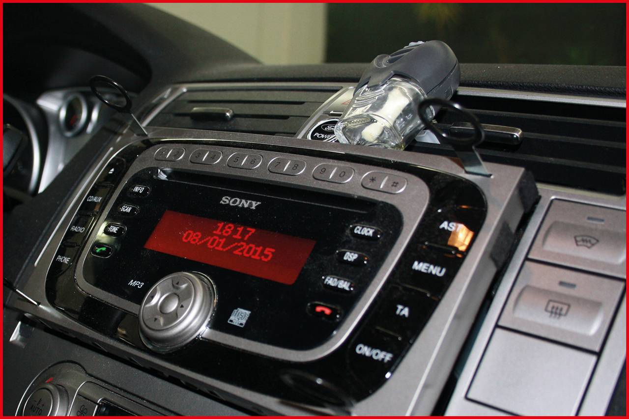 Autoradio mit Display zeigt '18:17 08/01/2015'. Steuerknöpfe für Lautstärke und Senderwahl sichtbar. In einem Auto installiert.