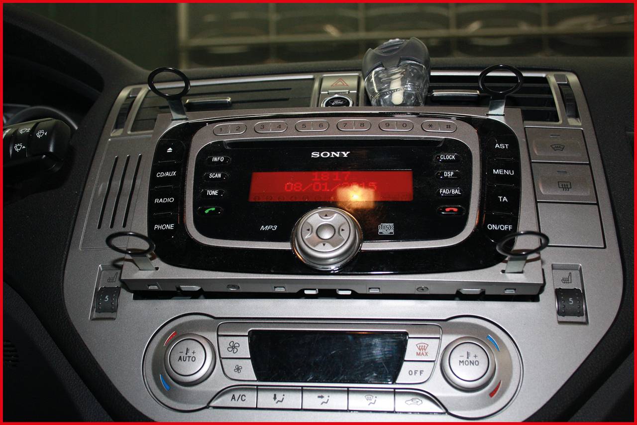 Autoradio mit großem Display in einem Auto-Dashboard. Tasten für Radio, MP3 und Lautstärke. Rotes Display zeigt 'AUS'. Klimaanlage unten.