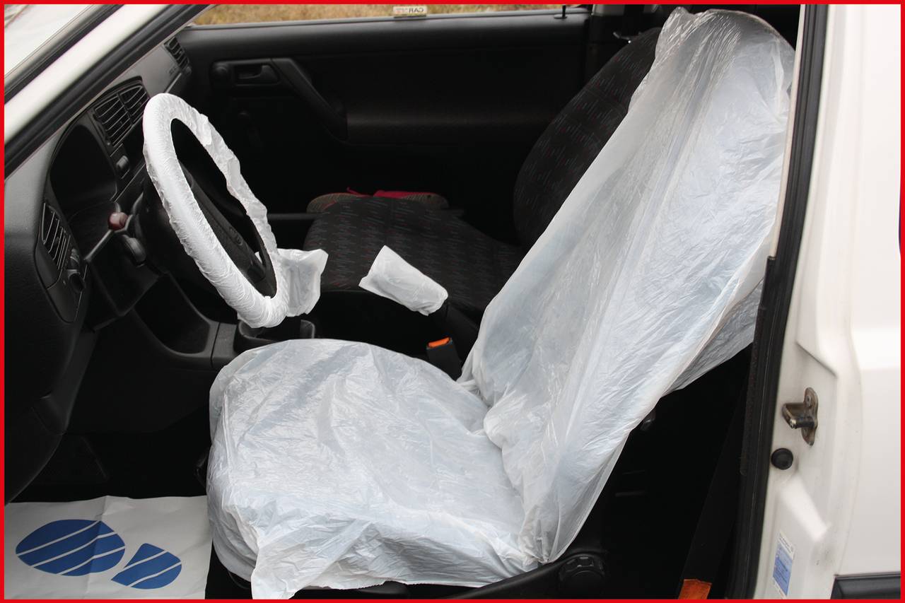 Das Bild zeigt den Innenraum eines Autos. Der Fahrersitz und das Lenkrad sind mit transparenten Plastikhüllen abgedeckt.