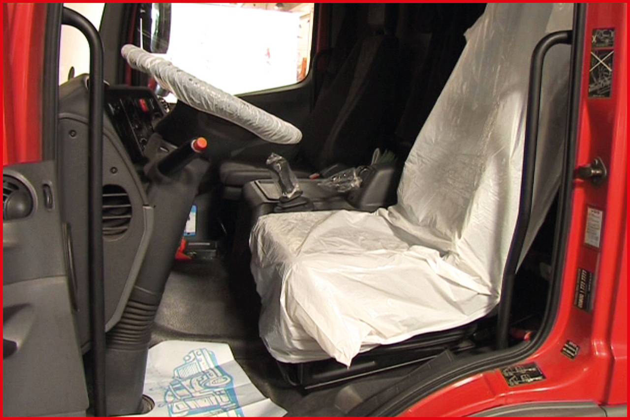 Innenraum eines großen Fahrzeugs, vermutlich ein Lkw. Der Fahrersitz ist mit einer Plastikfolie abgedeckt. Das Lenkrad hat ebenfalls eine Schutzhülle.