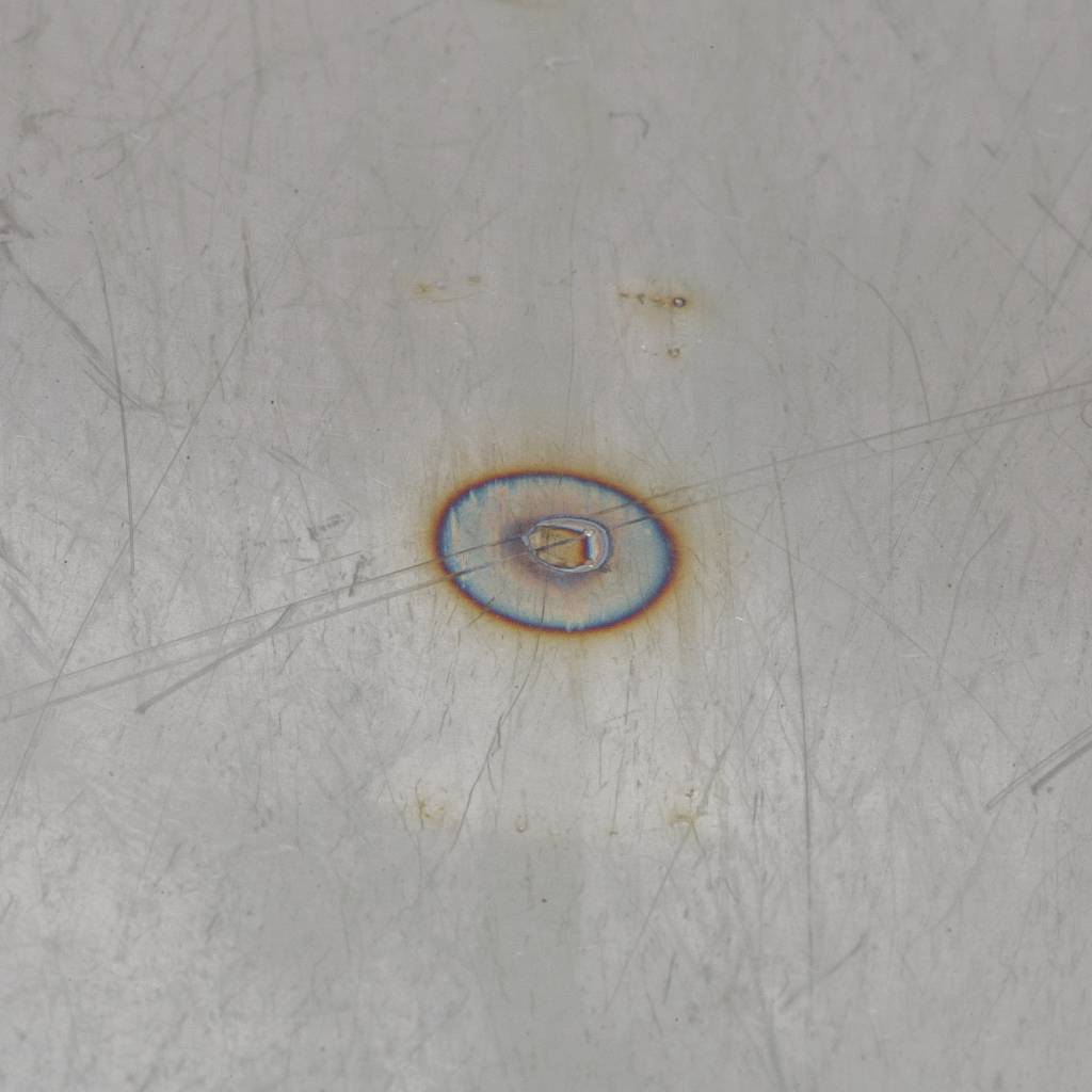 Eine Metalloberfläche mit einer kreisförmigen Verfärbung in der Mitte, die auf Hitzeeinwirkung oder Korrosion hindeutet.