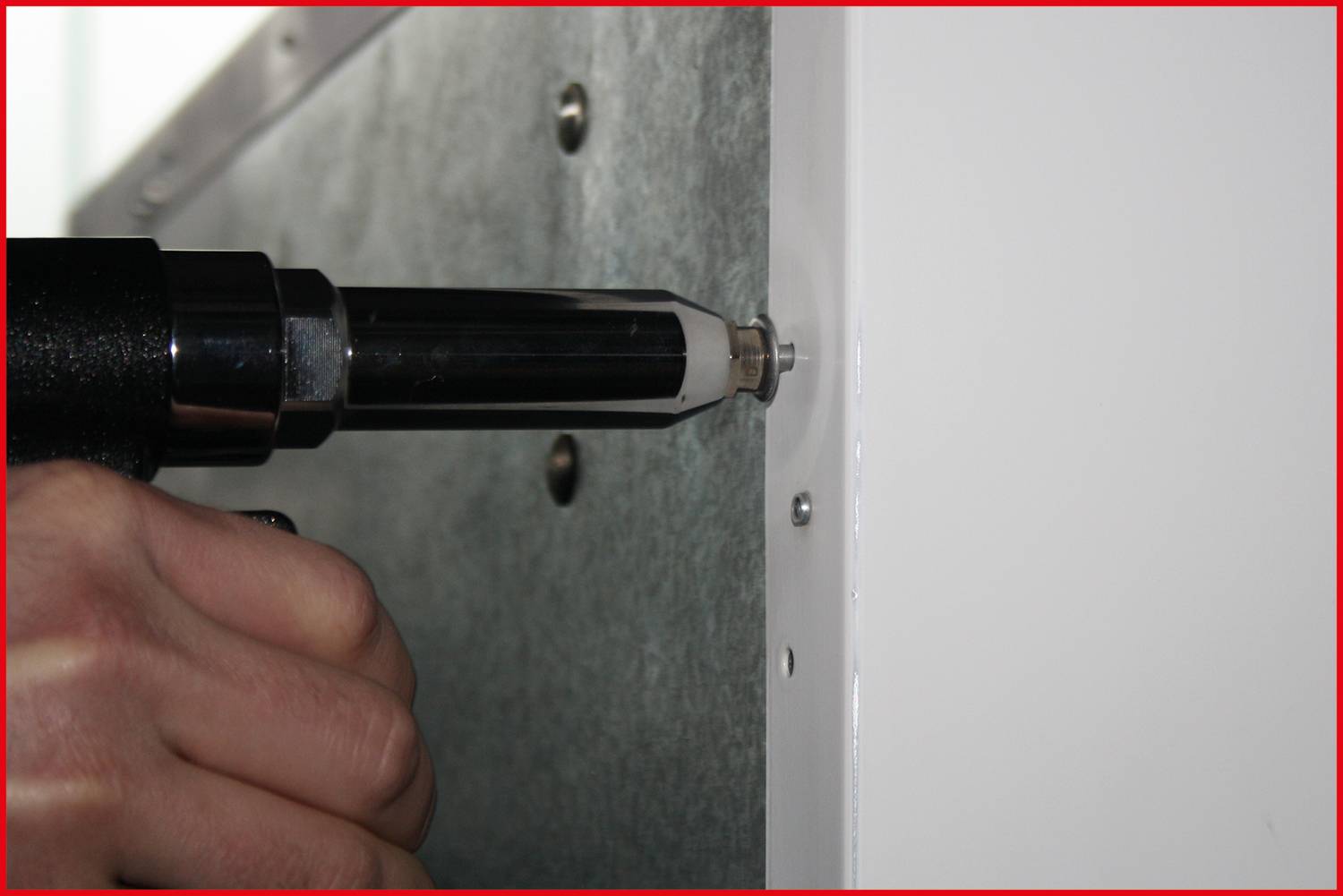 Eine Hand benutzt einen Druckluftschrauber, um eine Schraube in eine Metallplatte zu drehen.