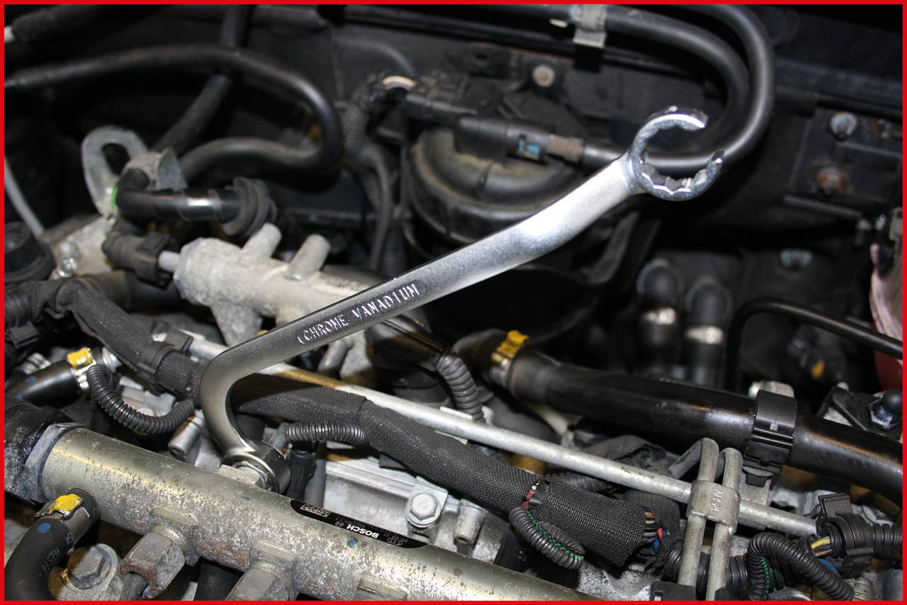 Ein Schraubenschlüssel liegt auf einem Automotor. Die Umgebung zeigt Kabel und Schläuche, typisch für einen Fahrzeugmotorraum.