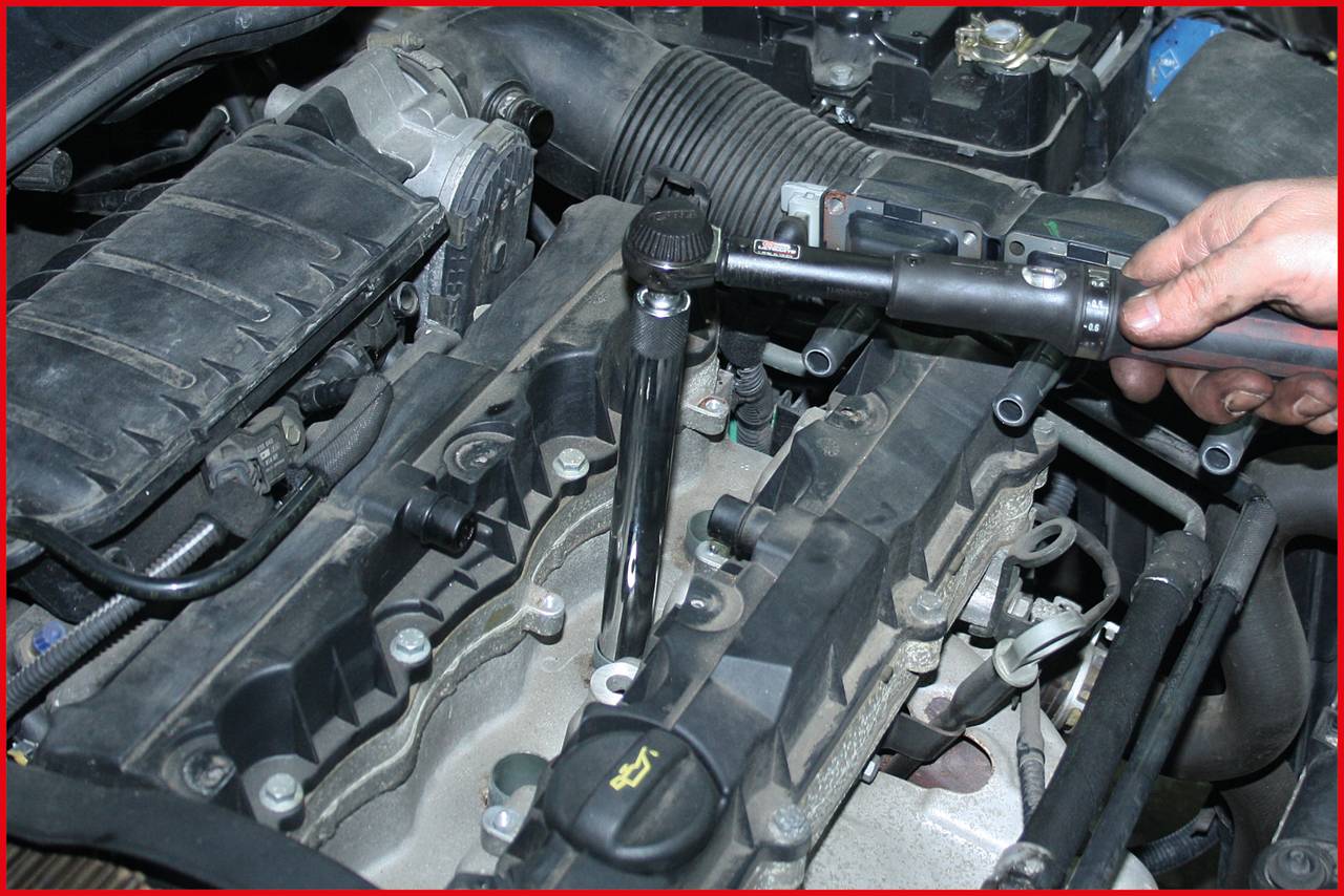 Eine Person repariert den Motor eines Autos. Ein Schraubenschlüssel wird verwendet, um eine Kerze im Motorraum anzuziehen.