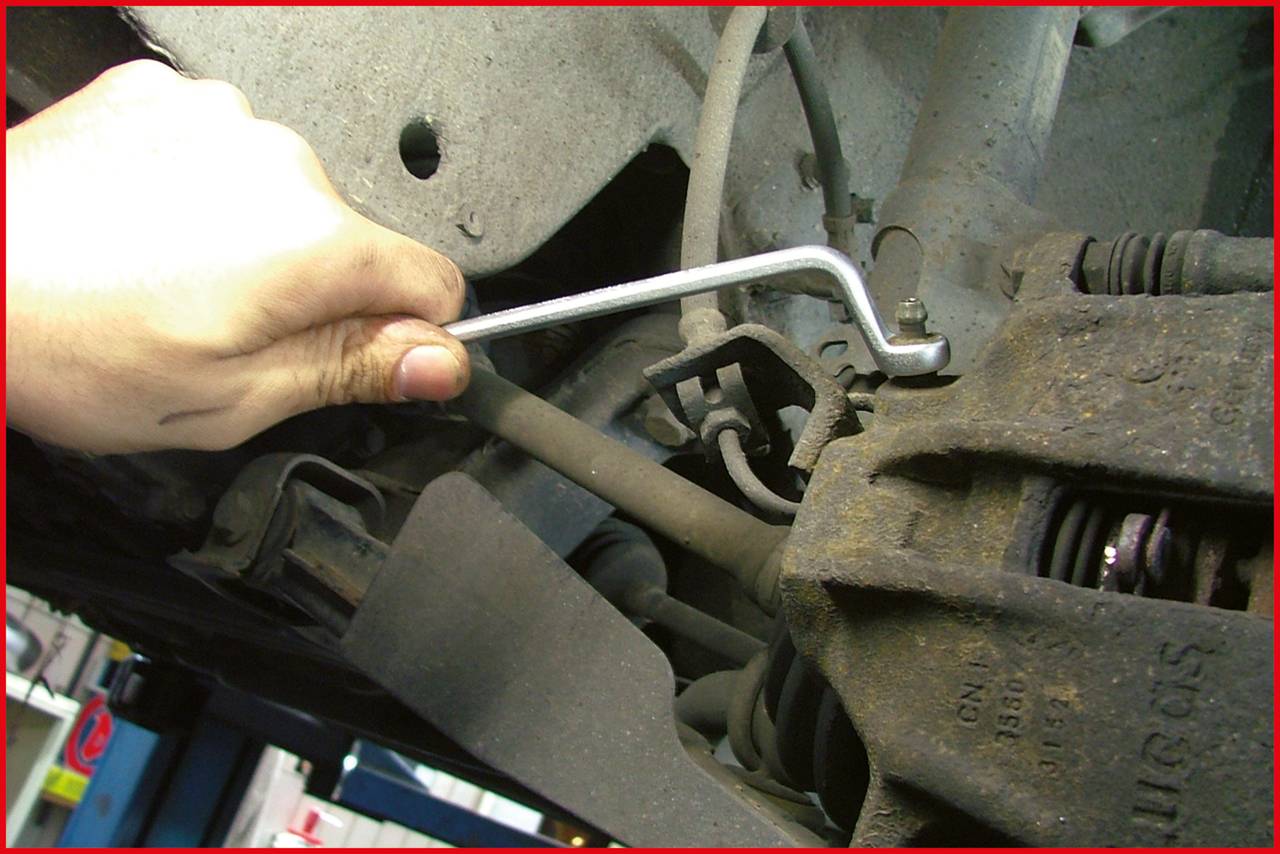 'Ein Mechaniker zieht mit einem Inbusschlüssel eine Schraube an der Bremsanlage eines Autos an.'