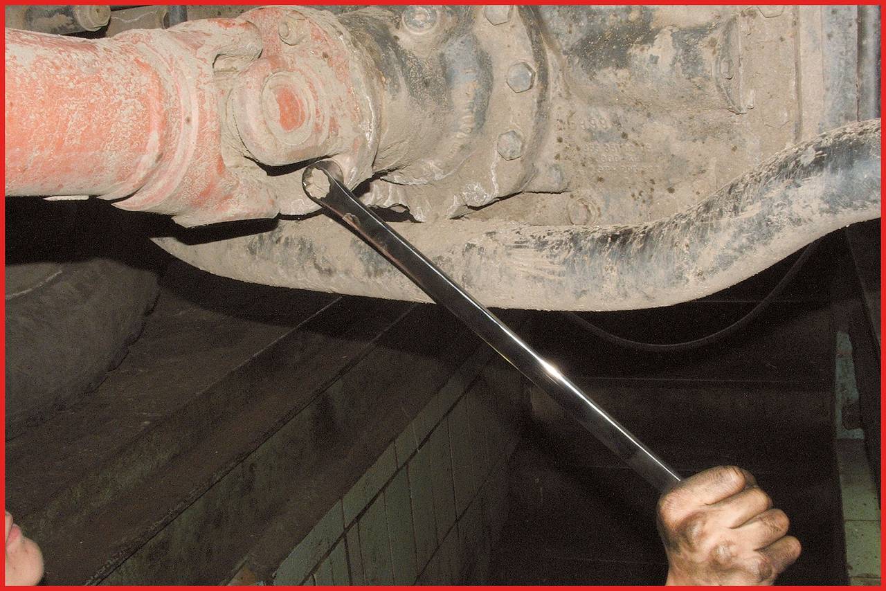 Eine Person zieht mit einem Schraubenschlüssel eine Schraube an einem mechanischen Teil fest. Die Umgebung wirkt industriell.