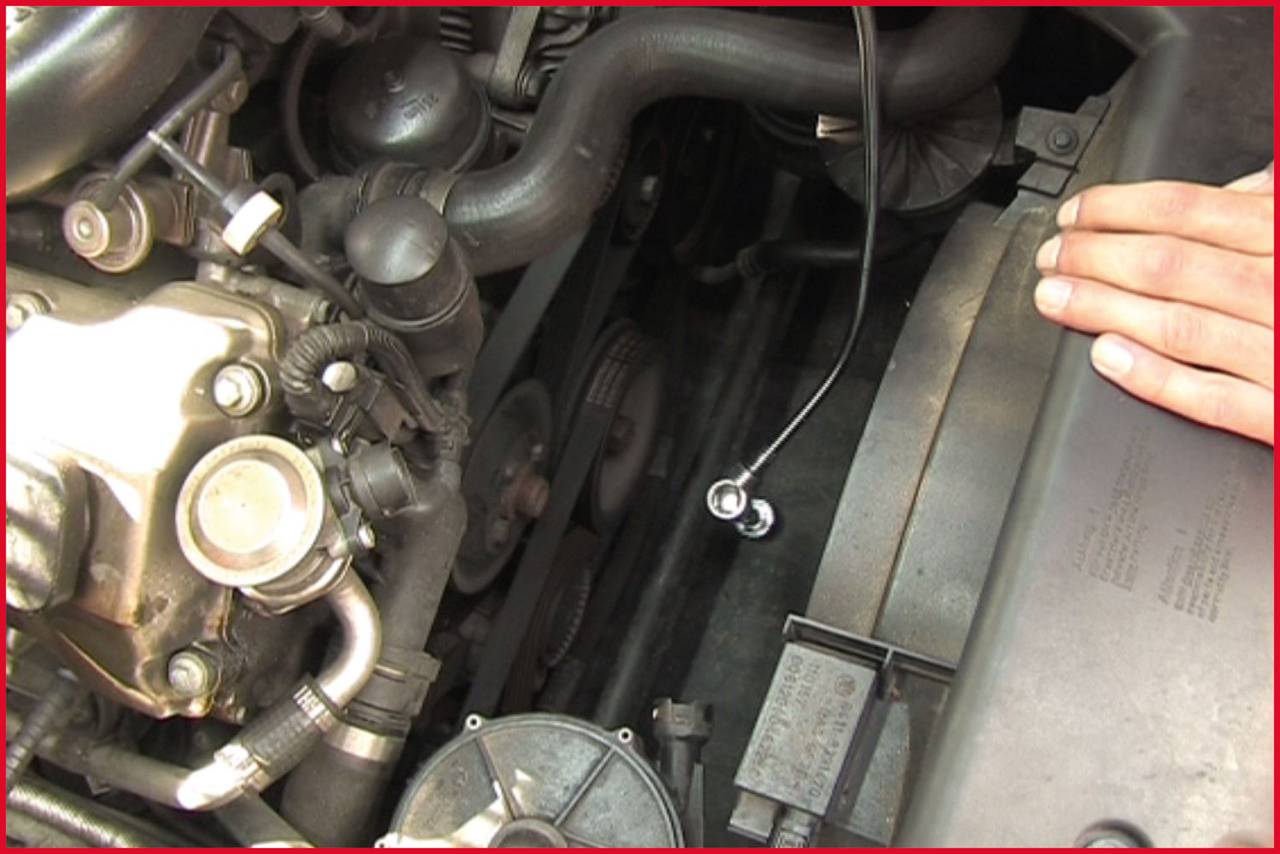 Nahaufnahme eines Automotors, wobei eine Hand rechts oben zu sehen ist. Ein Stethoskop wird zur Diagnose an den Motor gehalten.