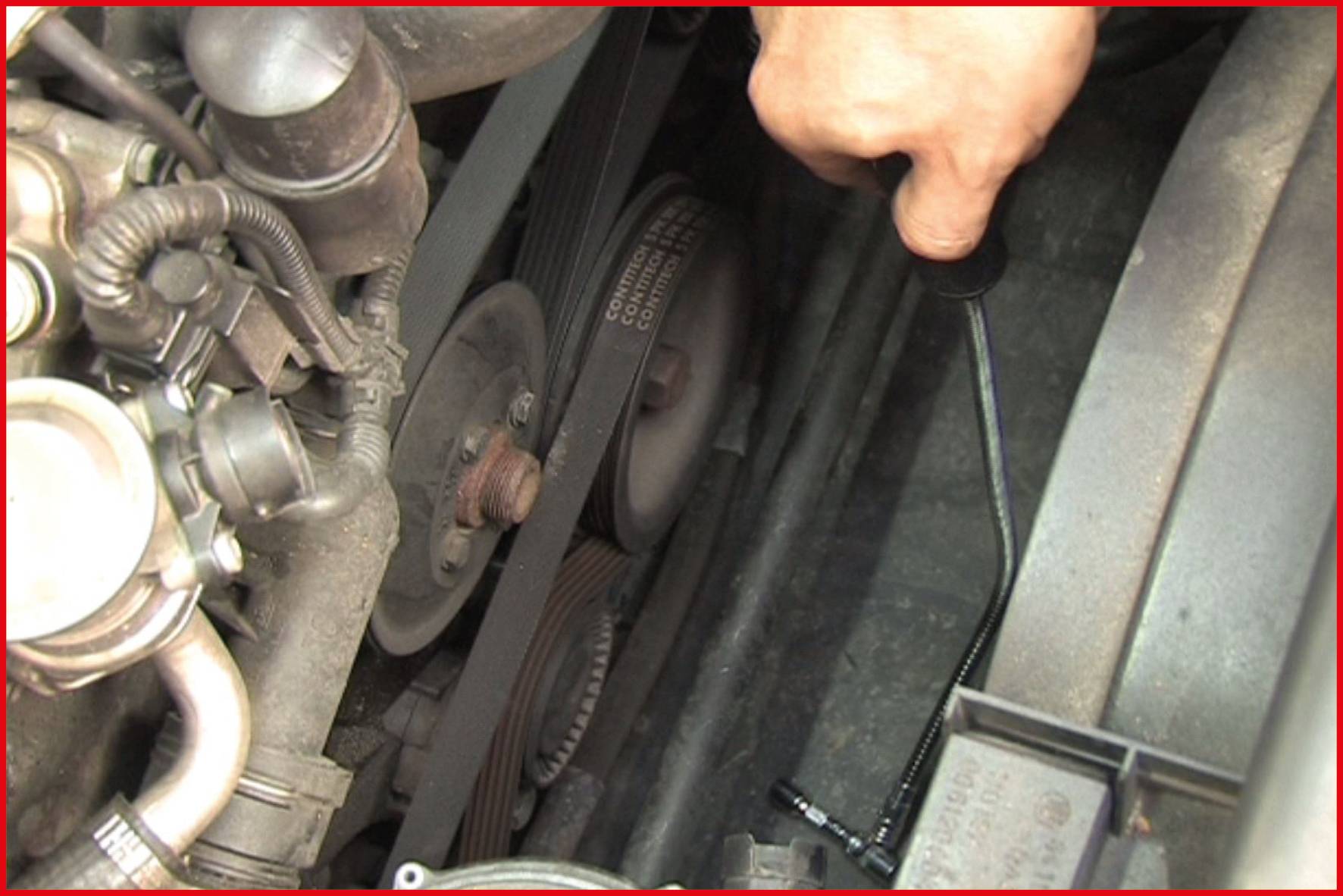 Ein Mechaniker überprüft den Keilriemen eines Automotors. Die Hand hält einen Schraubenschlüssel, um an einem Fahrzeugteil zu arbeiten.