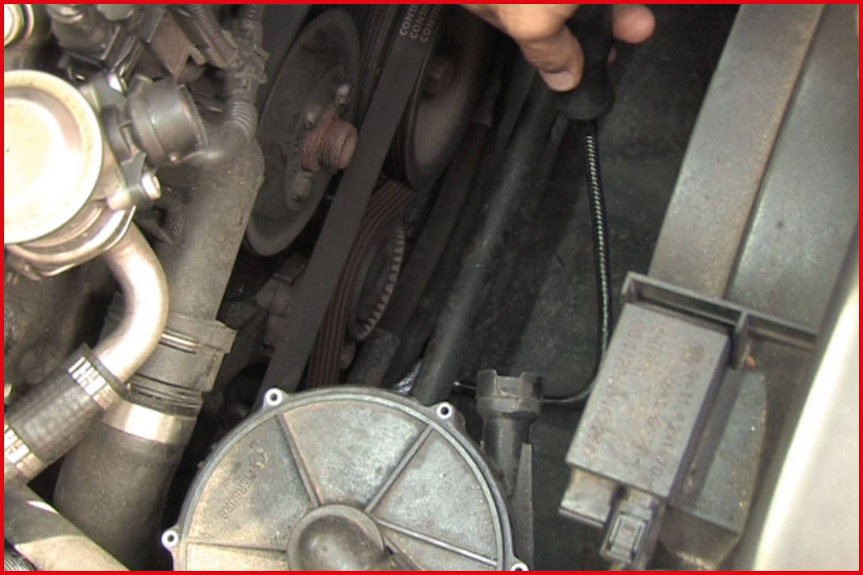 Eine Person überprüft mit einem Ölmessstab den Ölstand im Motorraum eines Autos. Im Bild sind Motorbauteile sichtbar.