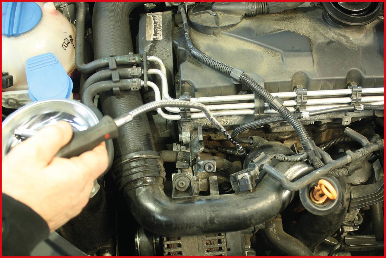 Eine Person prüft einen Motor mit einem Inspektionswerkzeug. Schläuche und Kabel sind sichtbar. Es handelt sich um eine Fahrzeugwartung.