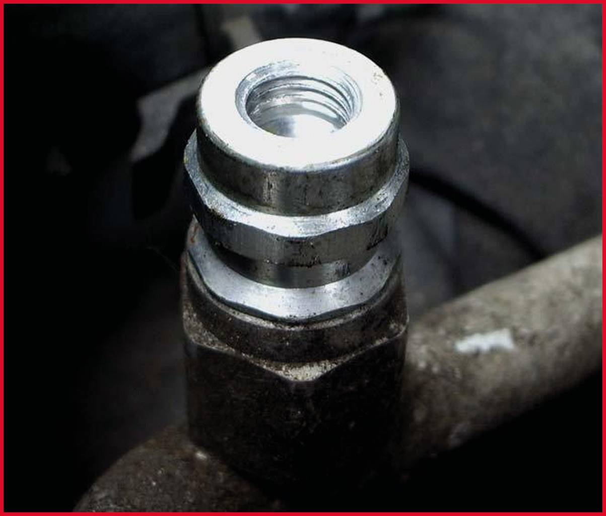 Nahaufnahme einer silbernen Metallverschraubung auf einer dunklen Oberfläche, möglicherweise ein Teil einer Maschine oder eines Fahrzeugs.