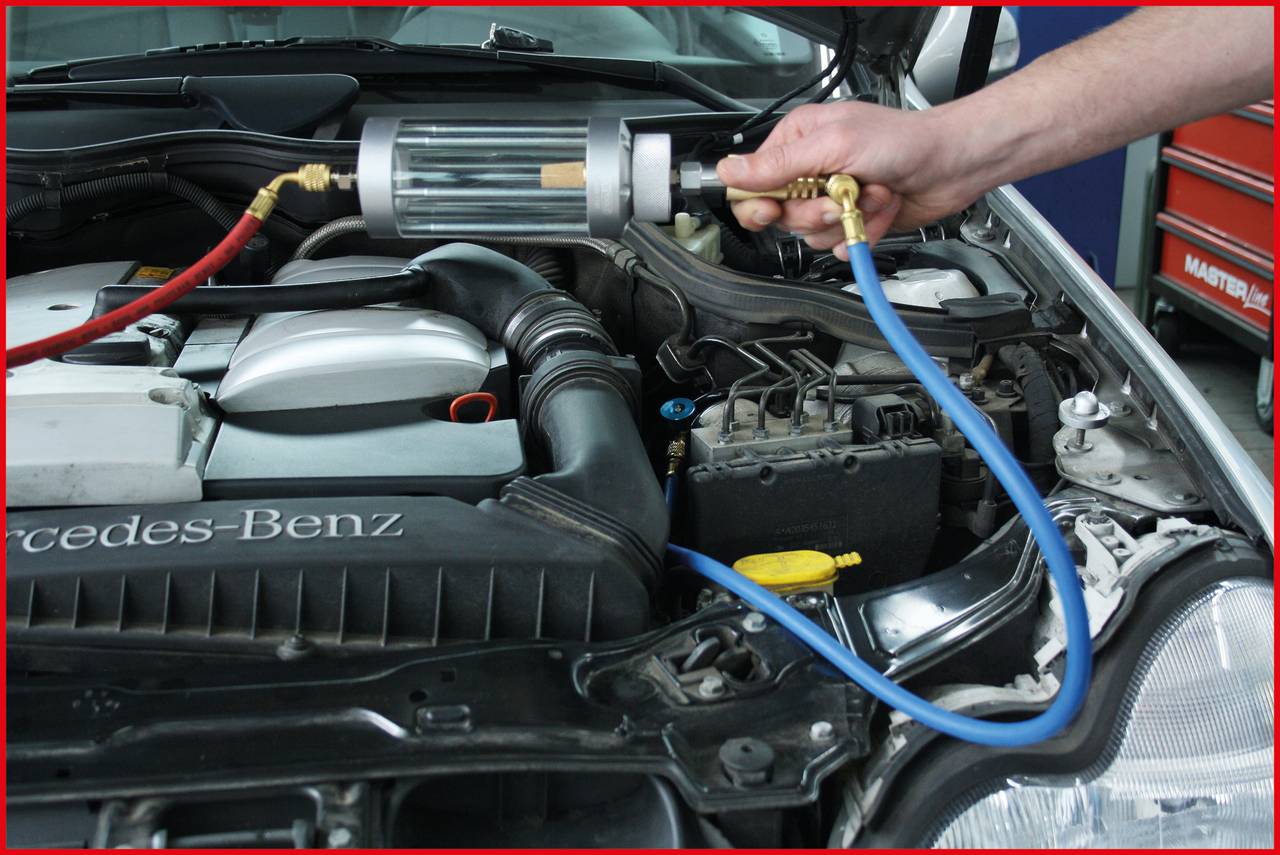 Ein Auto wird gewartet. Eine Hand hält ein Gerät mit Schläuchen über dem geöffneten Motorraum eines Mercedes-Benz.