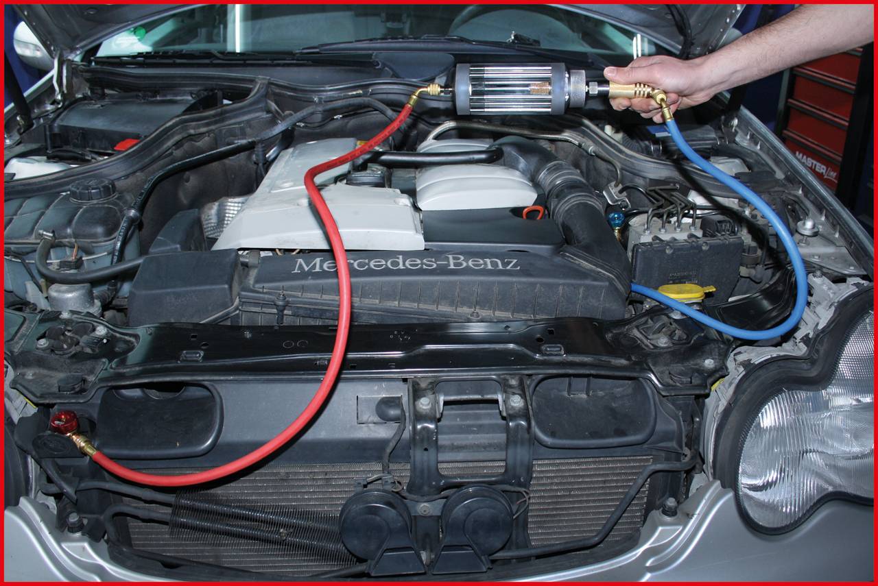 Ein Automechaniker prüft mit einem Diagnosegerät den Motor eines Mercedes-Benz in einer Werkstatt. Dabei sind Kabel angeschlossen.