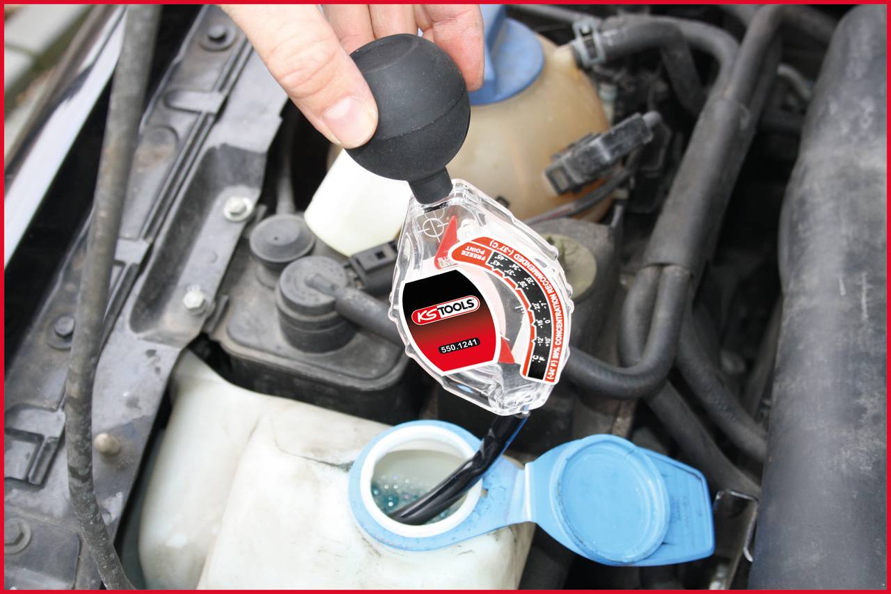 Hand hält Prüfgerät über einer offenen Kühlflüssigkeitsflasche im Auto. Das Prüfgerät misst den Zustand der Kühlflüssigkeit.