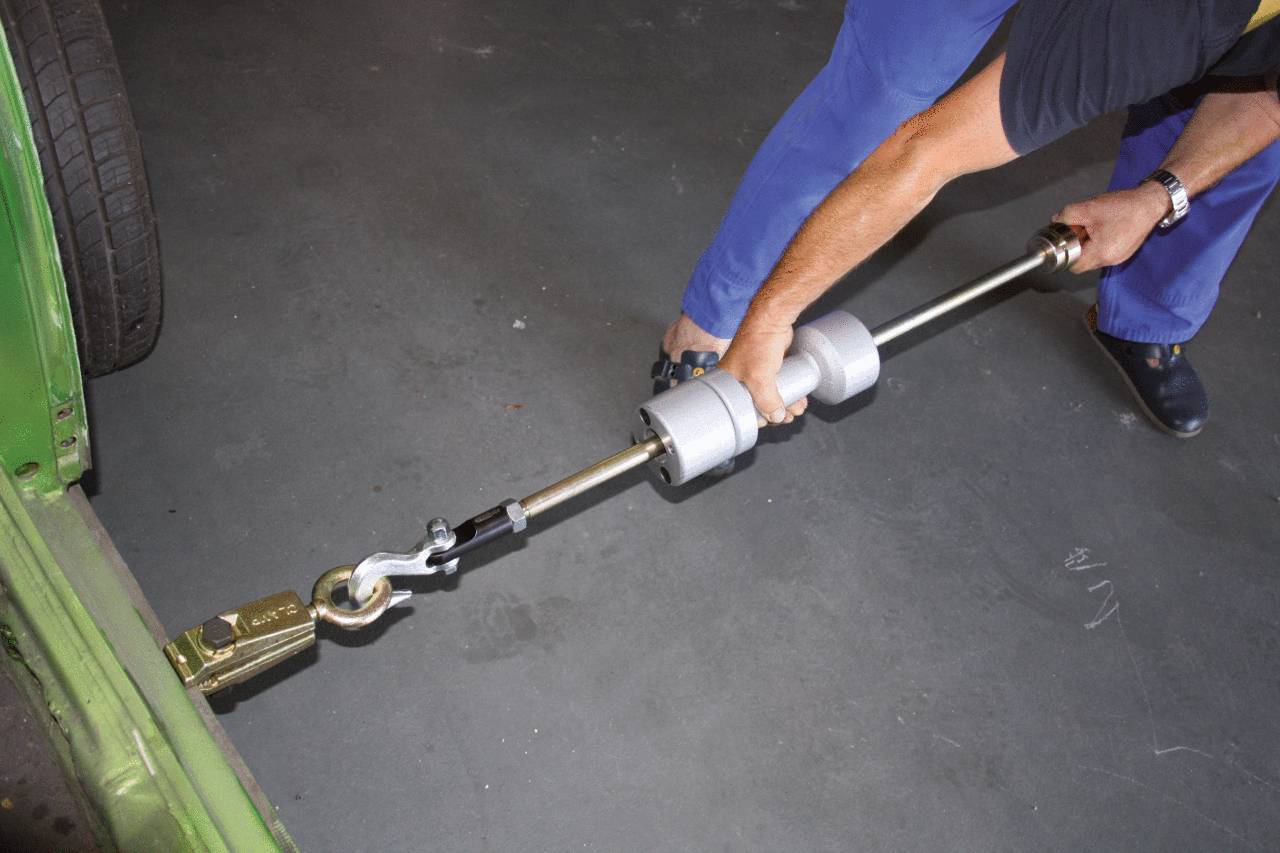 Person führt eine Autoreparatur durch, indem sie ein Zuggerät an einem Fahrzeug anbringt, um eine Karosserie- oder Rahmenbegradigung vorzunehmen.